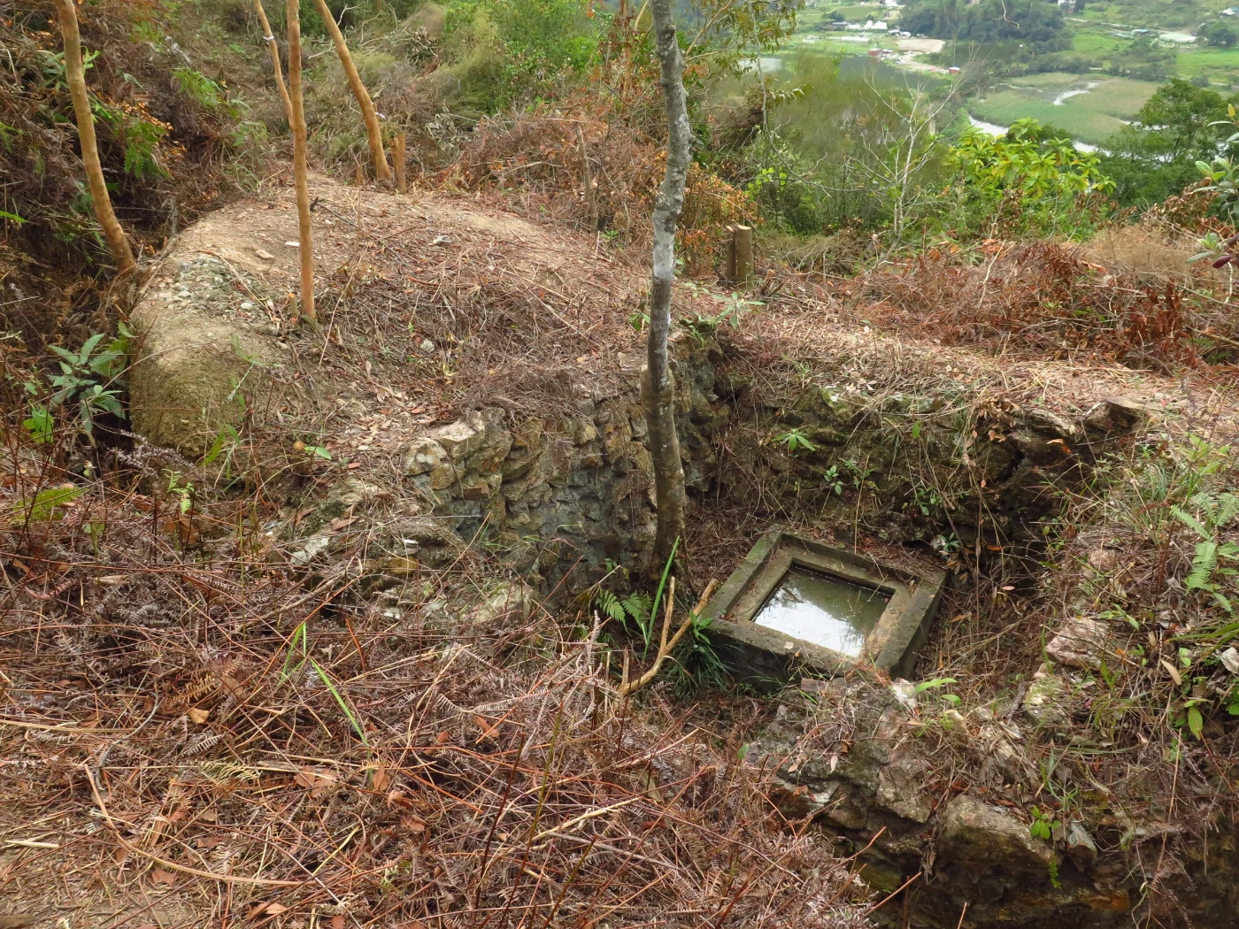 Inside a stone wall revetted enclosure, a 2-metre deep concrete shaft was constructed near a large rectangular pillbox close to the top of the knoll on the western side. Square in plan and with steel rungs for access on its southern side, its purpose has yet to be determined. Possible uses might have been water supply, field sanitation or some sort of shelter. (photo credit: The University of Hong Kong)
